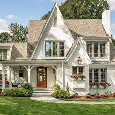 a white house with lots of windows and flowers on the front door, along with green grass