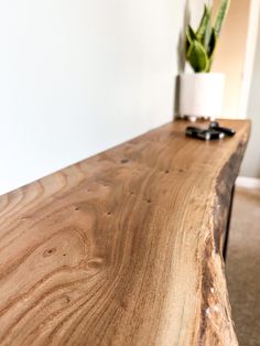 a close up of a wooden table with a potted plant in the corner behind it