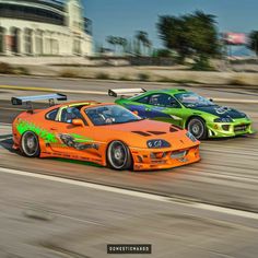 two orange and green sports cars driving down a race track in front of each other