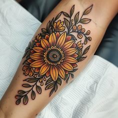 a sunflower tattoo on the arm with leaves and flowers around it's center