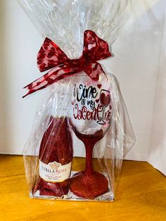 a wine glass and bottle wrapped in cellophane with a red bow on it