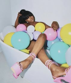 a woman sitting in a tub filled with lots of balloons and high heeled shoes