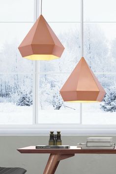 two pink lamps hanging from the ceiling in front of a window with snow on it