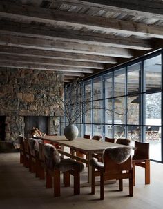 a dining room table with chairs and a fireplace in the back ground, surrounded by stone walls