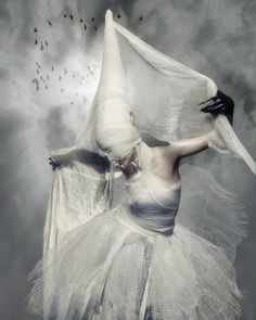 a woman in white dress flying through the air with her hands on her head and veil over her face