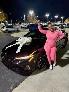 a woman in pink stands next to a black car with a white bow on it