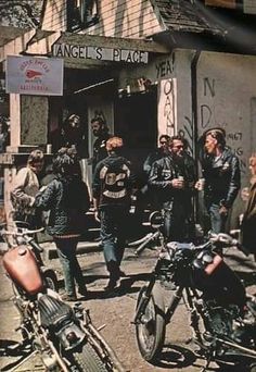 a group of people standing around motorcycles in front of a building with graffiti on it