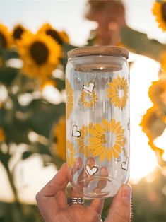 a person holding up a clear glass with sunflowers on it and hearts painted on the side