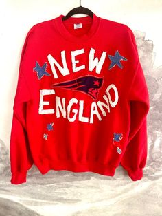 a red new england sweatshirt hanging on a white wall with the words new england printed on it