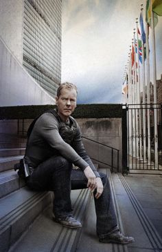 a man sitting on the steps in front of a building with flags flying above him