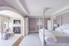 a bedroom with purple walls and white bedding, fireplace in the corner and large mirror on the wall