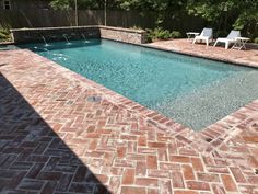 an empty swimming pool surrounded by brick pavers and chairs with trees in the background