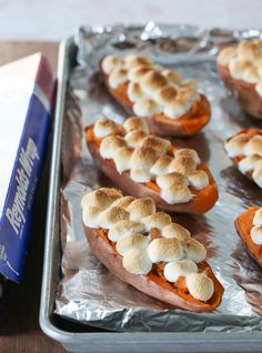 baked sweet potatoes topped with marshmallows on a baking sheet next to a book