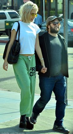 a man and woman walking down the street holding hands, both wearing green sweatpants