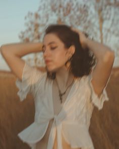 a woman standing in a field with her hands on her head and wearing a white top