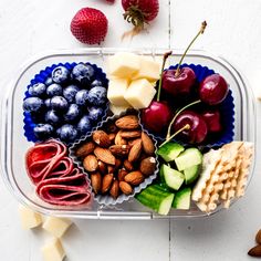 a plastic container filled with assorted fruits and crackers on top of a white table