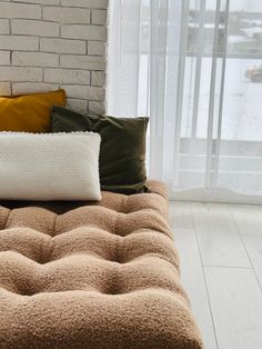 a couch with pillows on top of it in front of a brick wall and window