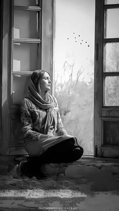 a woman sitting on the ground in front of an open window looking at the ocean