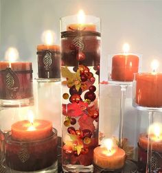 candles are arranged in glass vases with leaves and berries on the bottom one candle is lit