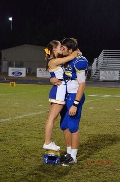 two people are hugging each other on a football field at night with rain falling down