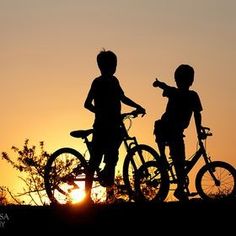 two children are standing with their bikes at sunset