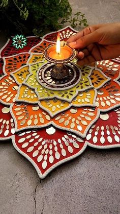 a person holding a lit candle on top of a colorful flower shaped plate with dots