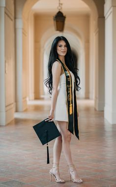 a woman standing in an archway with her hand on her hip wearing a black and gold graduation stole