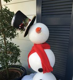 a snowman with a hat and scarf on it's head is standing in front of a house