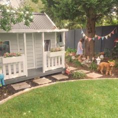 a woman standing next to a dog in a yard with a tree and flower potted plants