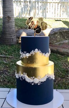 a blue and gold wedding cake sitting on top of a white platter in front of a palm tree