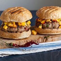 two hamburgers with meat and pineapple are on a cutting board