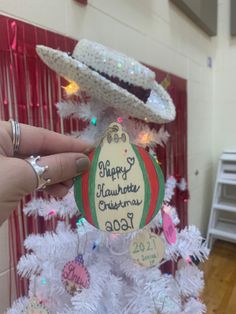 someone holding up a christmas ornament in front of a white tree