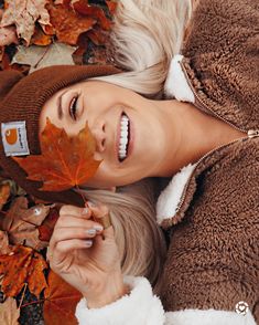 a woman laying on the ground with a leaf in her hand and wearing a brown jacket