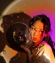 a woman holding a disco ball in front of a purple and pink background with the light reflecting off her face