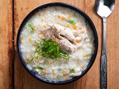 a bowl filled with rice and meat on top of a wooden table next to a spoon