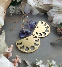 "These lovely, lightweight earrings feature beautiful, top-grade Fluorite gems with shades of purple, lavender, clear, and aqua and sparkly, lilac crystals. The flashy gemstones are finished with a warm brass, half-circle charms with cutouts of the phases of the moon. They measure approximately 2\" long x just under 1.25\" wide and the earwires are hypo-allergenic, 10kt gold-filled. Please note: these earrings are made-to-order and there may be slight variations from pair to pair. Thanks for che Celestial Amethyst Moon Phase Jewelry, Celestial Moon Phase Amethyst Jewelry, Purple Bohemian Everyday Jewelry, Adjustable Purple Moon Phase Jewelry, Celestial Purple Dangle Earrings, Purple Celestial Dangle Earrings, Purple Adjustable Celestial Jewelry, Adjustable Purple Celestial Jewelry, Handmade Purple Moon-shaped Jewelry