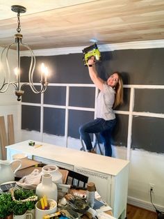 a woman standing on top of a white table in front of a gray wall with windows