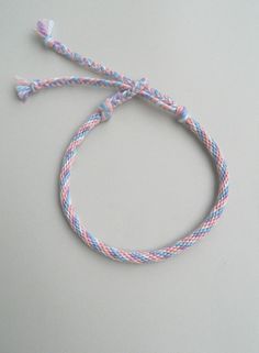 a blue, pink and white braided bracelet on a gray surface with an orange tag hanging from it's end