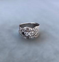 This unique ring is crafted from a vintage silver spoon, specifically the "Distinction 1951 Prestige Plate" pattern by Oneida Silver Flatware. The intricate detailing and timeless elegance of this pattern are beautifully preserved in the ring's design. The silver has been meticulously polished and shaped, creating a piece that is both charming and durable. Ideal for those who appreciate the blend of history and craftsmanship, this ring makes a distinctive statement while offering a touch of vint Vintage Flower Ring With Intricate Design For Promise, Vintage Silver Filigree Ring, Vintage Sterling Silver Filigree Ring, Vintage Engraved Silver Ring, Vintage Silver Engraved Ring Gift, Vintage Silver Engraved Ring As Gift, Vintage Silver Engraved Ring For Gift, Handmade Vintage Sterling Silver Filigree Ring, Vintage Silver Flower Ring Gift