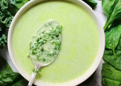 a white bowl filled with broccoli soup next to some green leafy greens