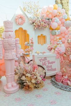 a table topped with lots of pink and white balloons next to a small toy house