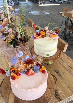 two cakes sitting on top of a wooden table covered in flowers and greenery next to each other