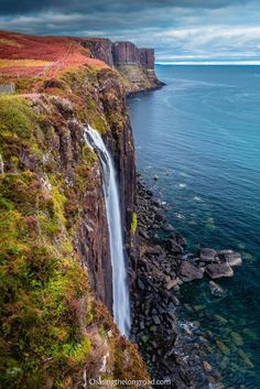 a waterfall in the middle of a body of water next to a cliff with trees on it