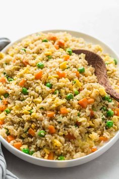 a white bowl filled with rice and vegetables on top of a table next to a wooden spoon