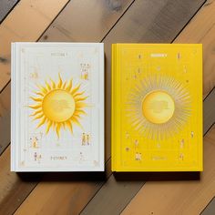 two notebooks sitting on top of a wooden floor next to each other, one with an image of the sun