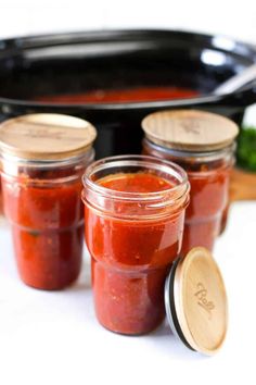 four jars of tomato sauce sitting in front of a slow cooker