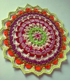 a crocheted doily is displayed on a white surface with orange, pink and green colors