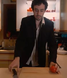 a man in a black jacket cutting tomatoes on a wooden counter top with a knife