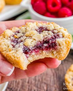 a hand holding a berry crumb cookie over a wooden table with raspberries in the background