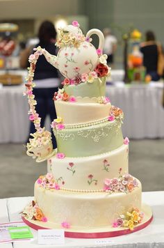 a three tiered wedding cake with flowers on the side and a tea pot on top